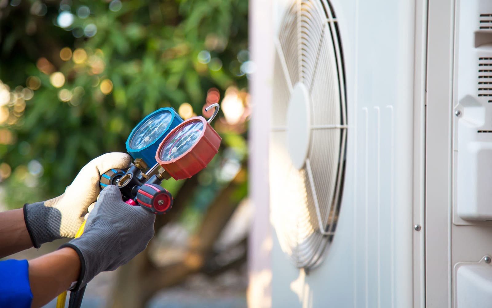 An HVAC technician checking refrigerant on a residential air-conditioning compressor unit