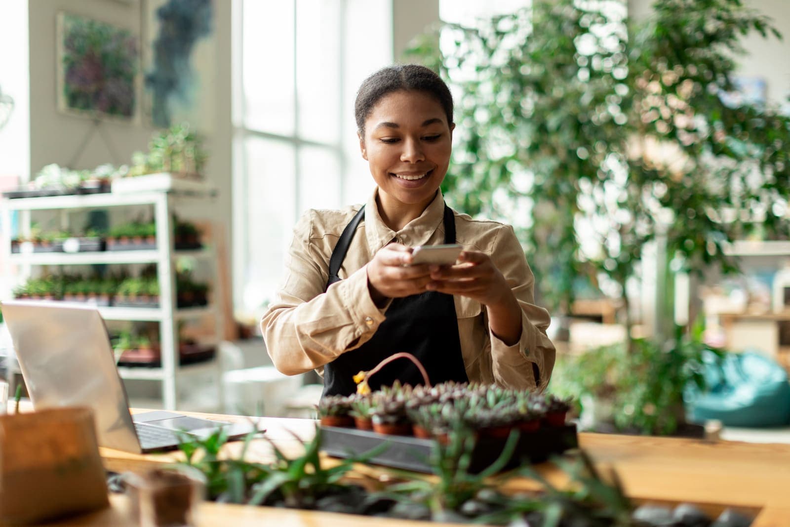 Small business owner photographing her products on a phone for social media inside her plant shop