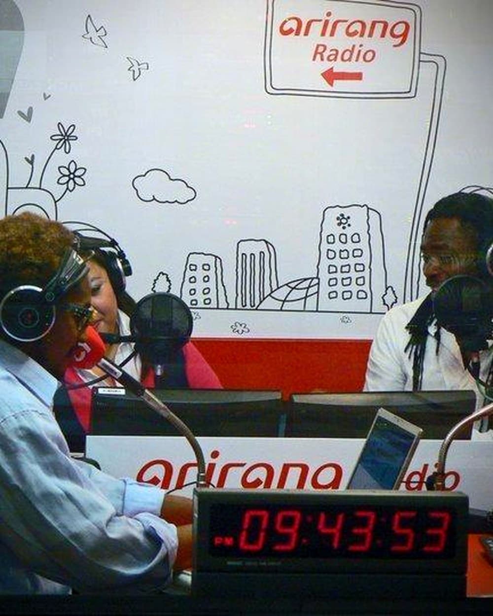 Roger Wong Won hosting at Arirang Radio's studio in Seoul, the Arirang Radio mural behind the on-air desk