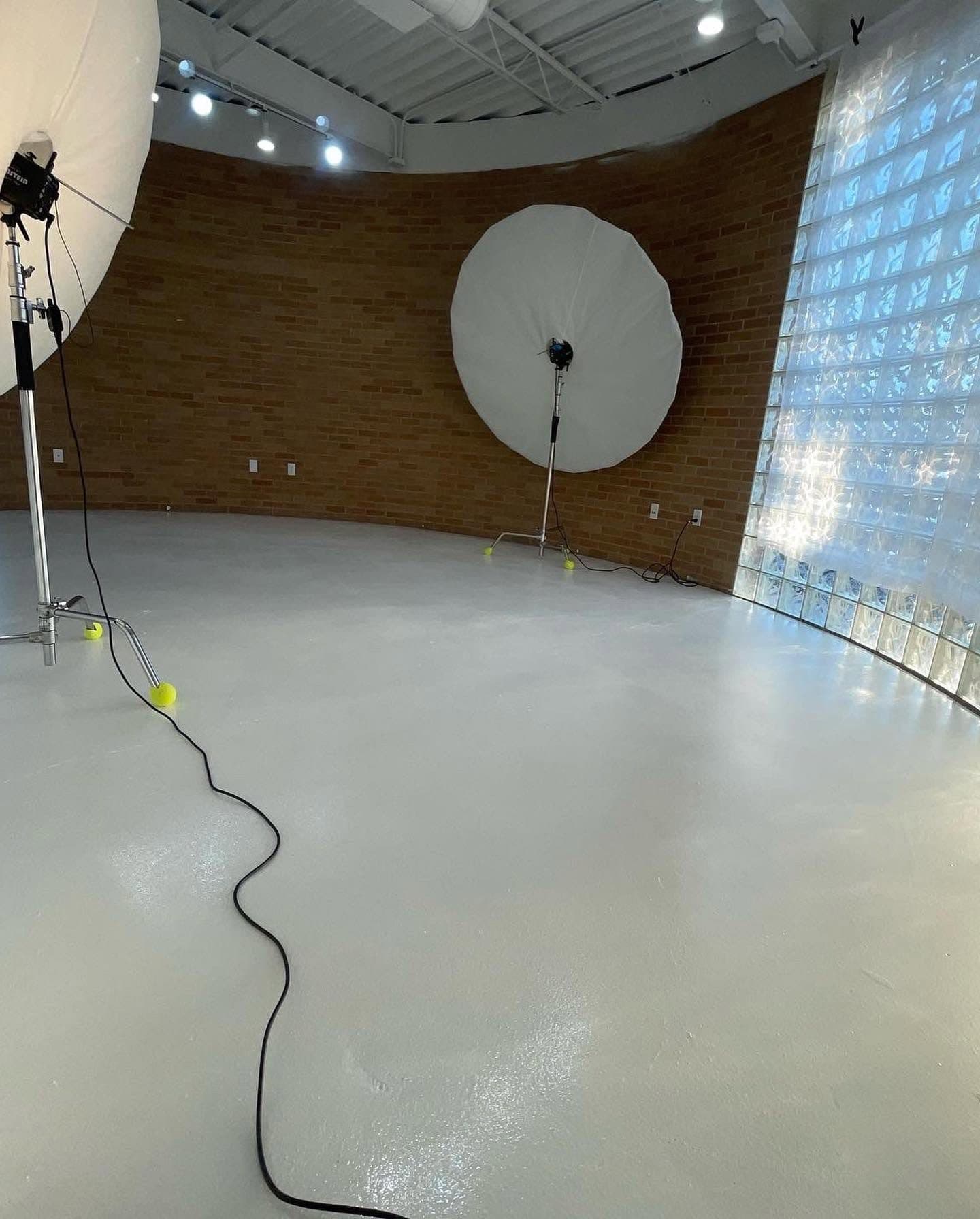 The main studio at San Antonio Studios, painted white floor, brick walls, glass-block window, and professional lighting umbrellas