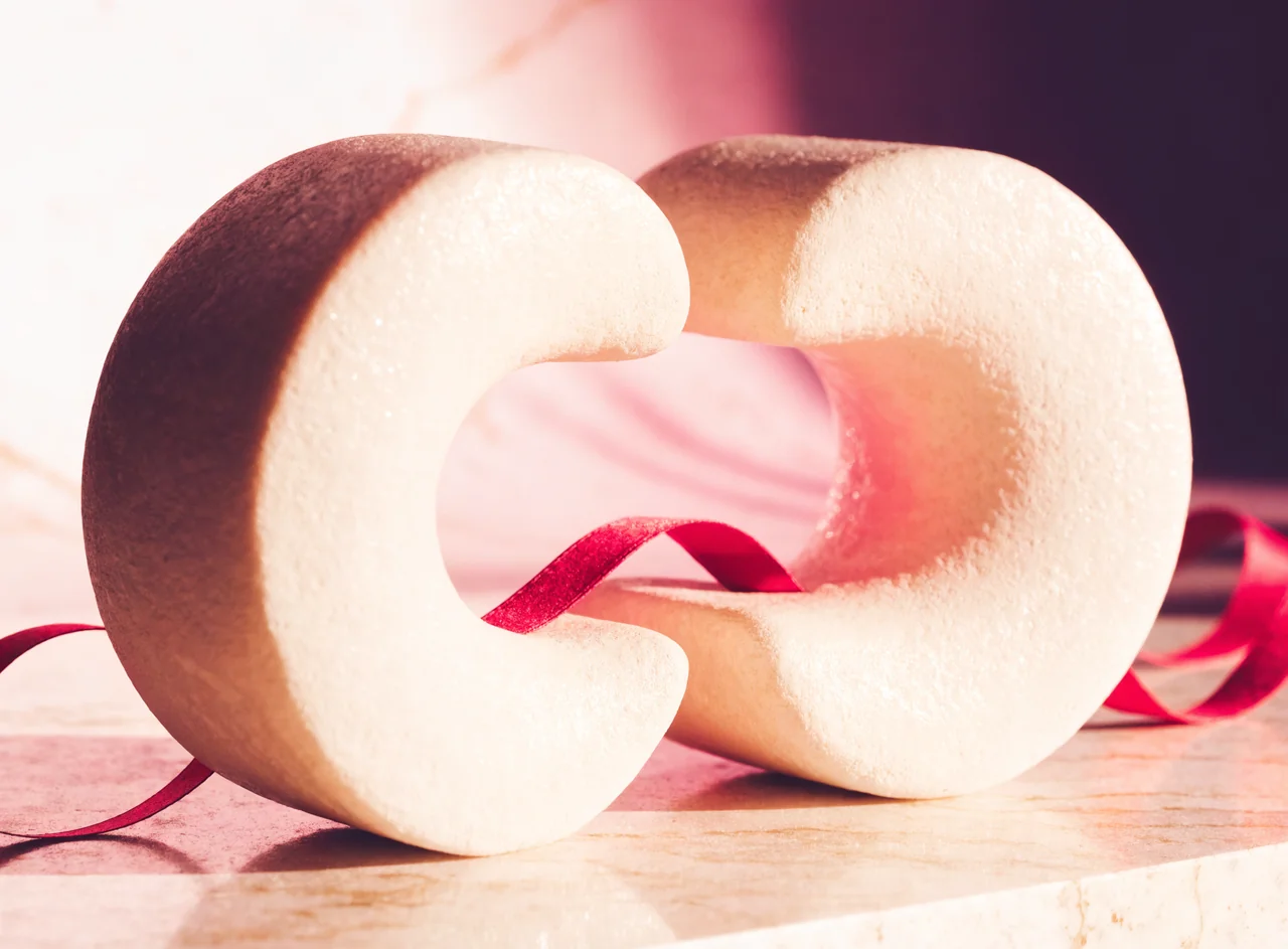 Two curved ceramic sculptures linked by a raspberry ribbon.